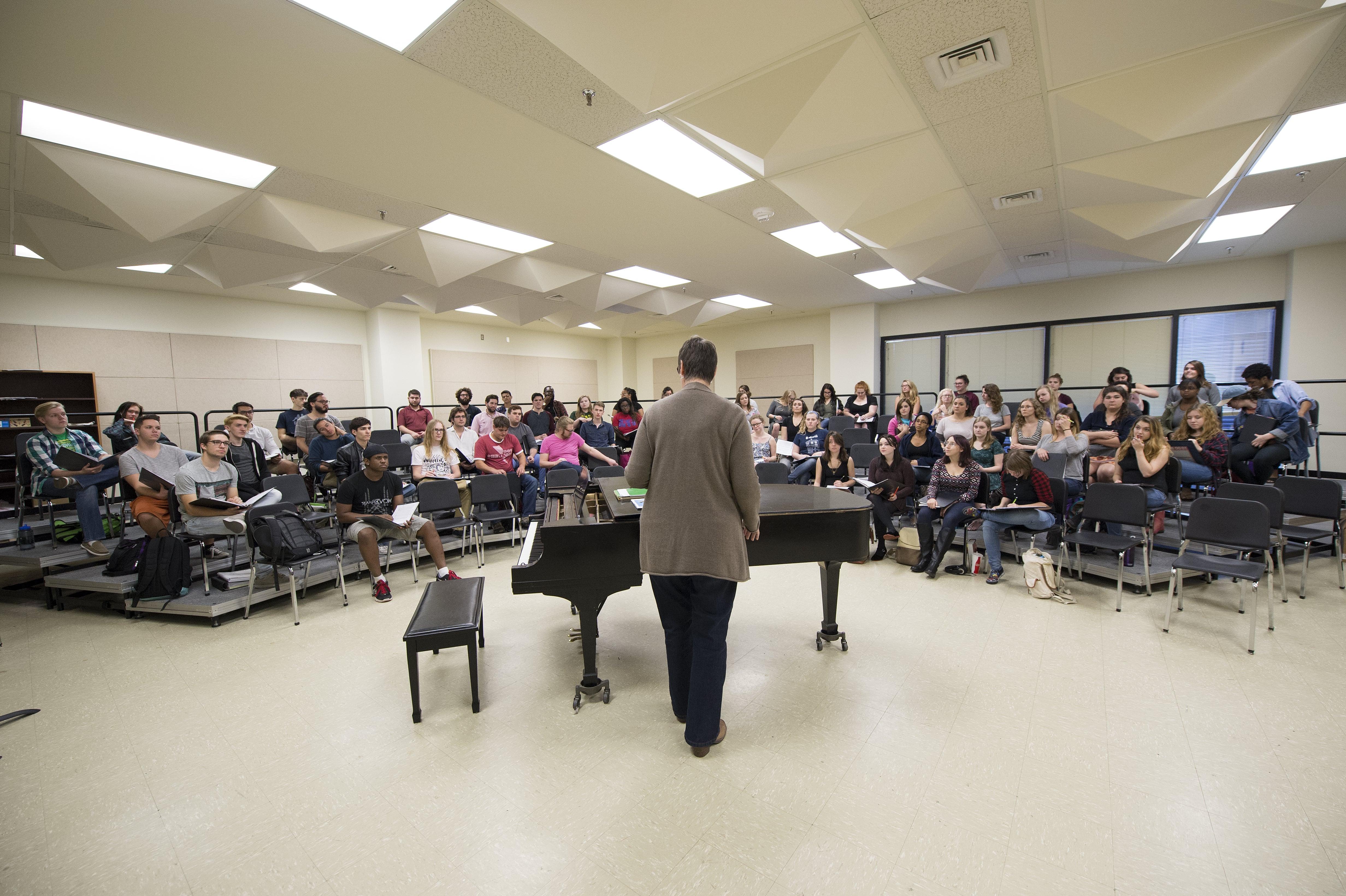 A wide shot of a large Loyola choir rehearsing in the choir room.